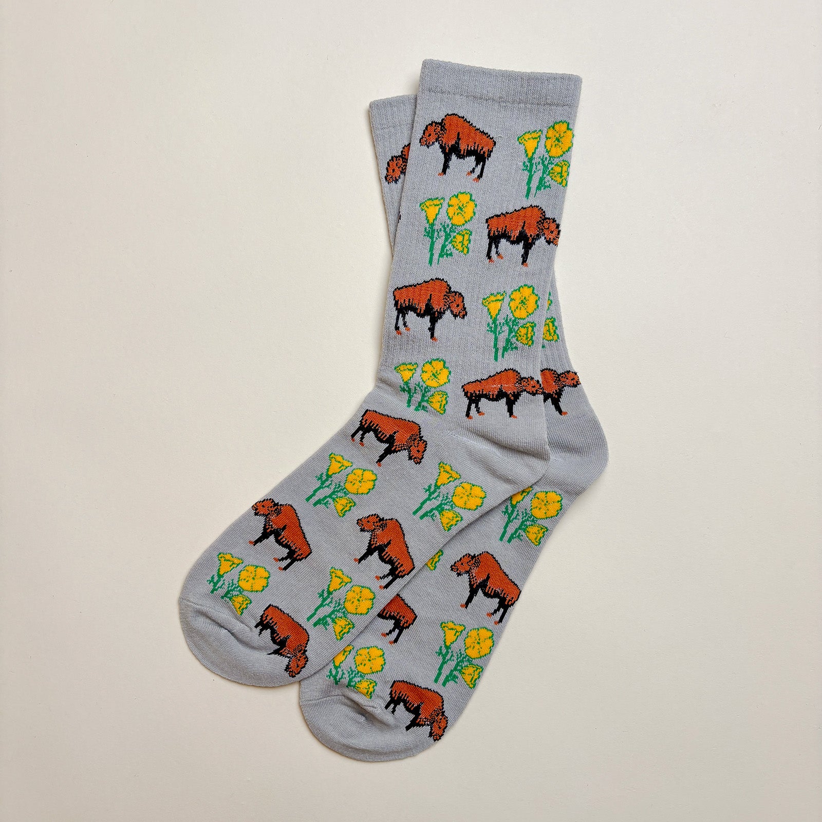 A pair of gray socks with a repeating animal print pattern of bison and california poppies.